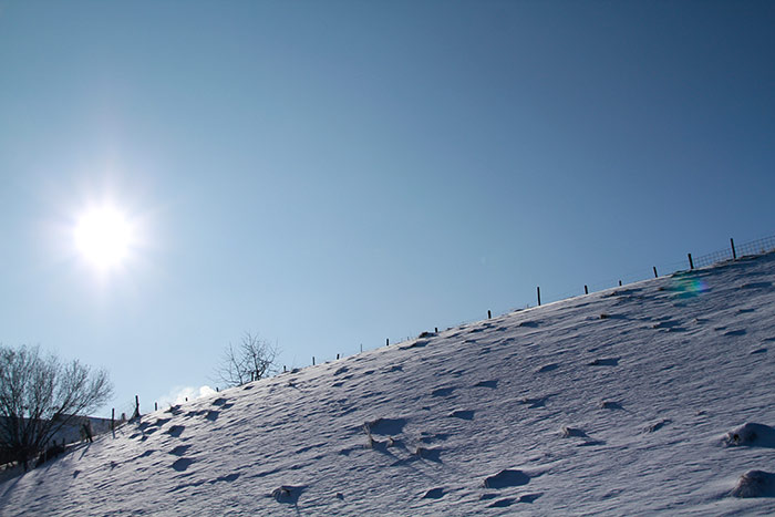 Schneefeld, Zaun, Sonne am blauen Himmel
